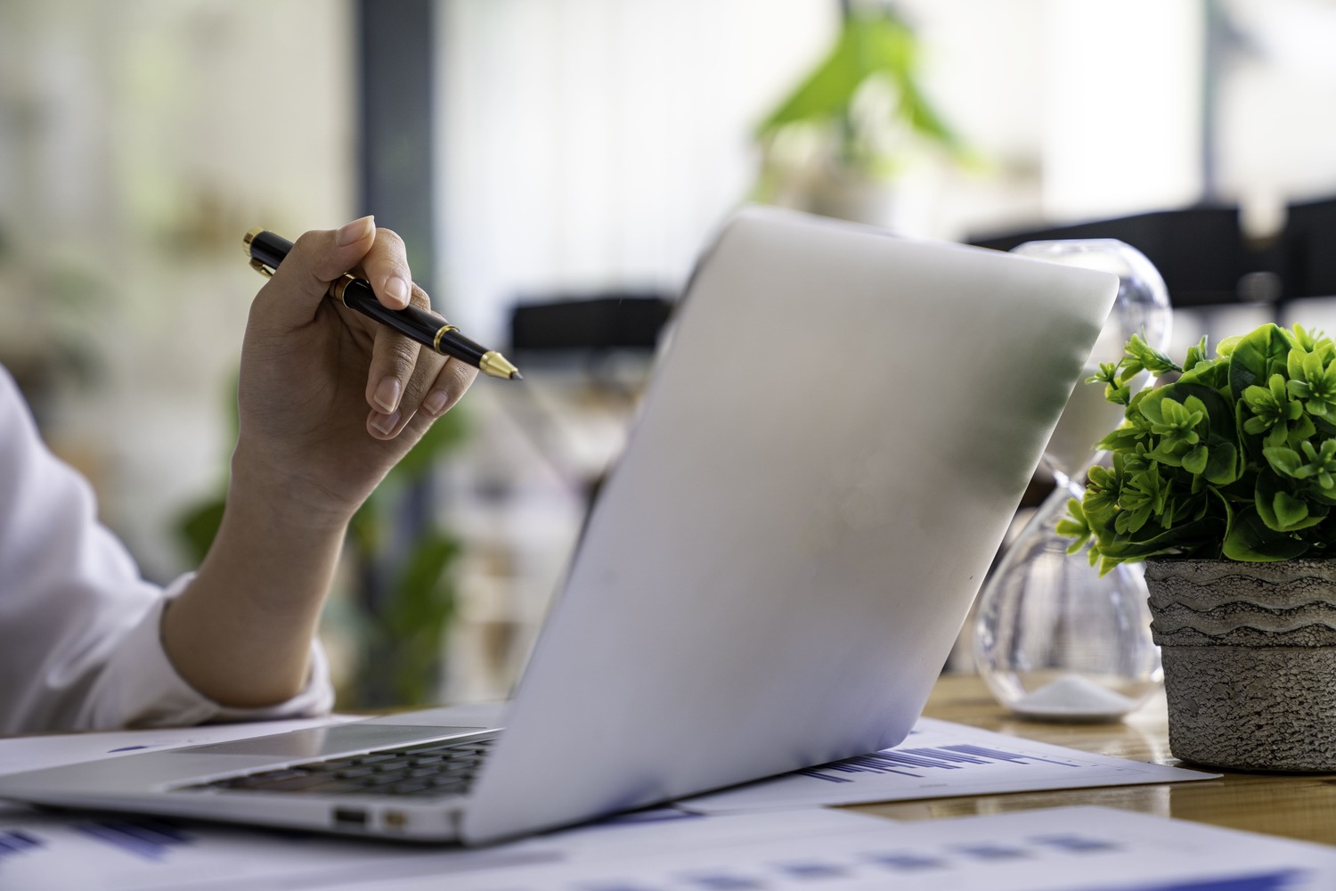 Parte de tras de um notebook em cima de uma mesa, homem mexendo na tela com uma caneta