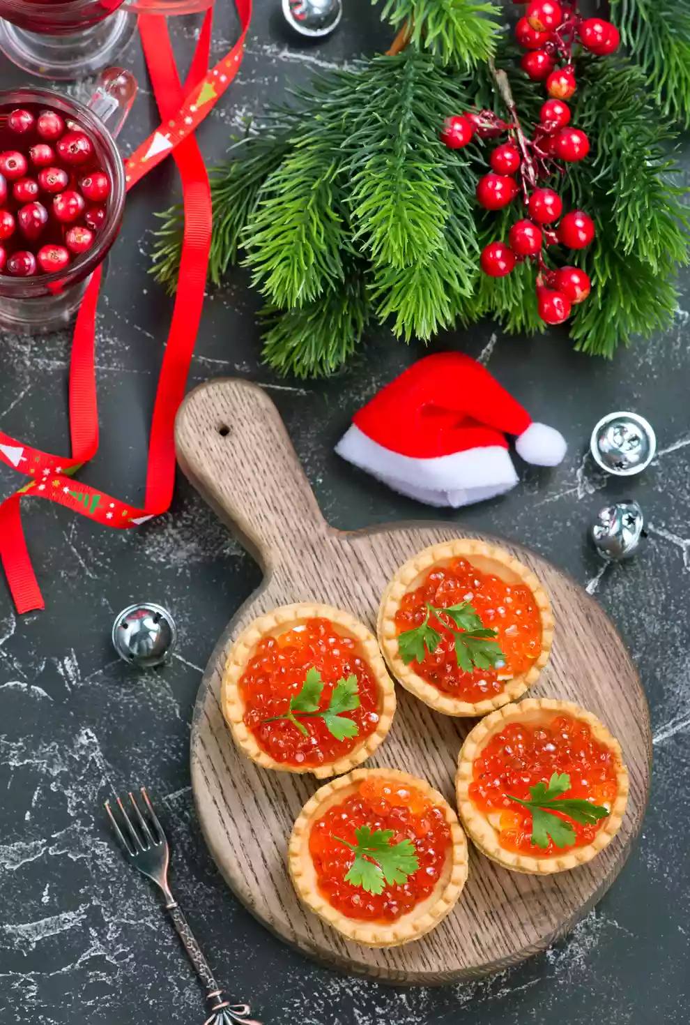 Mesa com gorro de papai noel, galhos de árvore de natal e uma taboa de comida com quatro tortinhas em cima