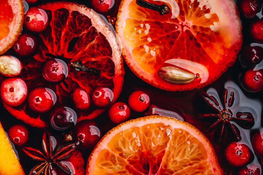 Imagem vista de cima de várias frutas cortadas como laranjas e frutas vermelhas todas cobertas por uma calda vermelha