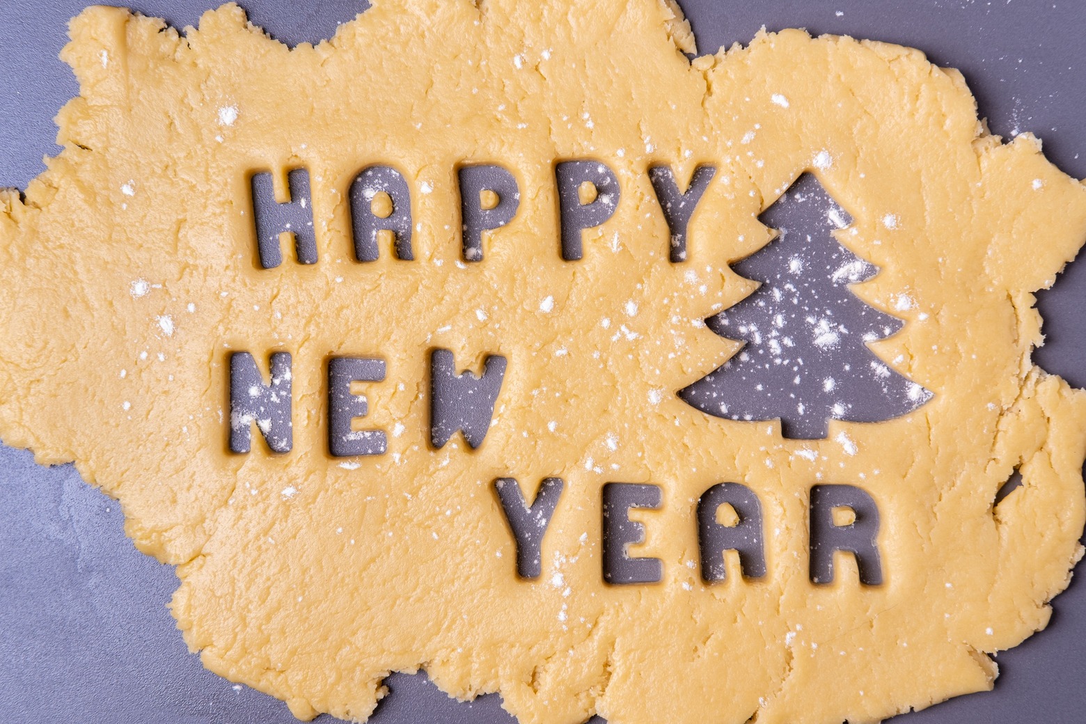 Recorte em massa de biscoito em forma de texto Feliz Ano Novo e árvore de Natal polvilhada com farinha