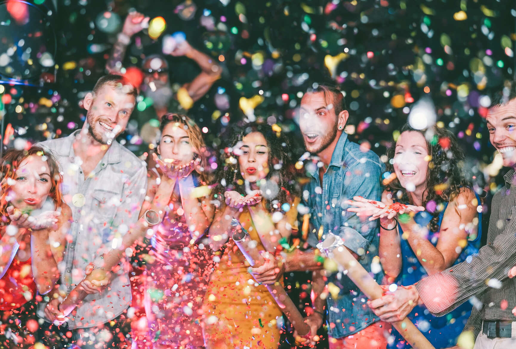 Grupo de amigos rindo e soltando confetes em festa