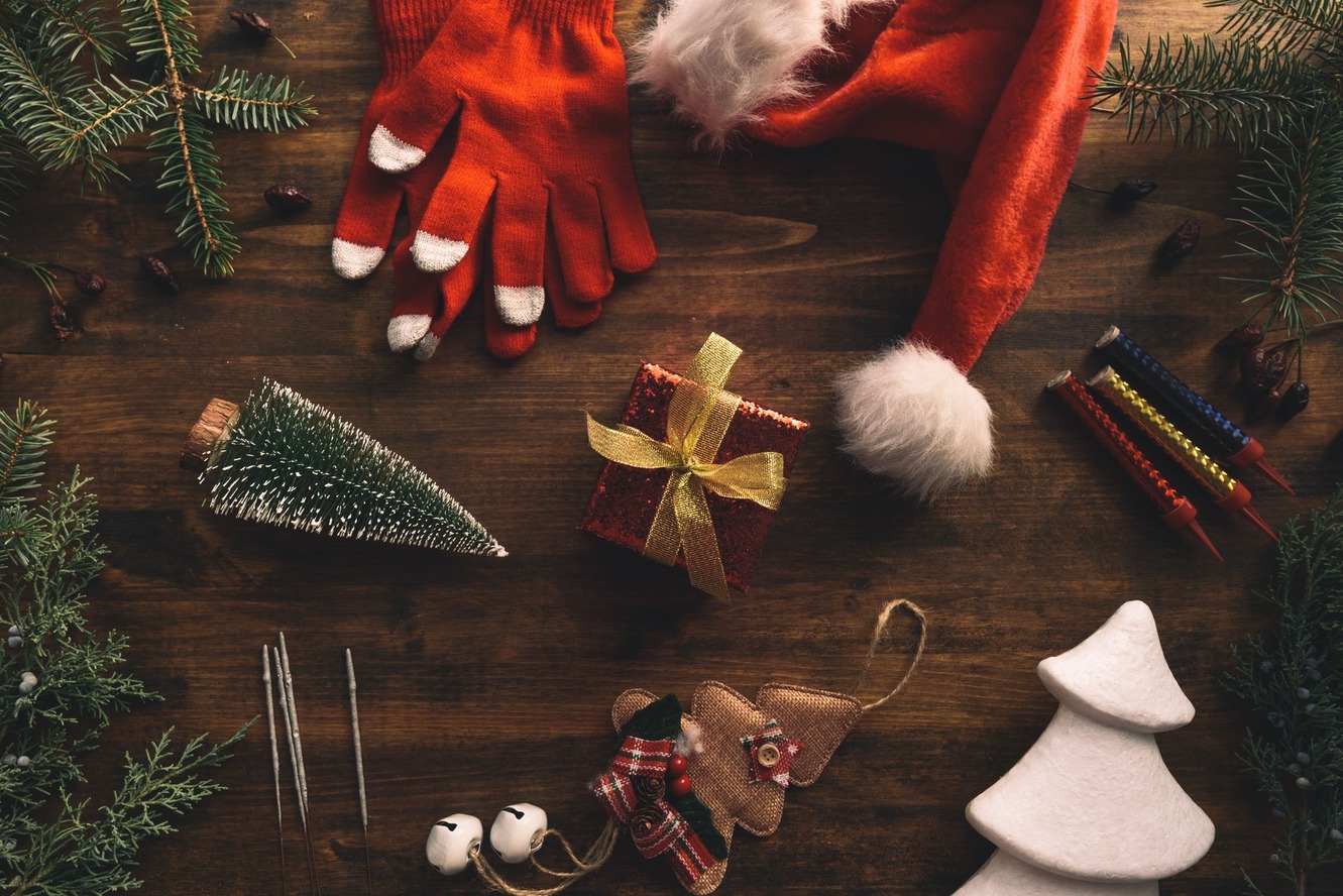 Uma pequena caixa de presente vermelha com laço dourado no centro, ao redor diversos enfeites de natal