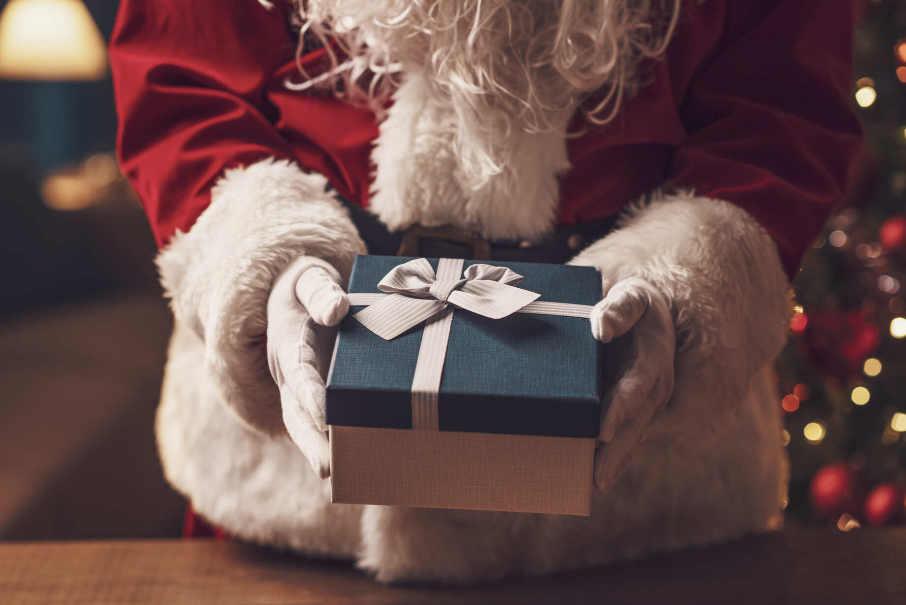 Braços e troco do papai noel enquanto ele segura um presente na caixa branca e azul com faixa branca