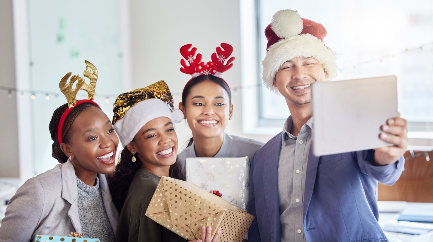 Um grupo de 4 colegas tirando uma selfie enquanto comemoram o Natal no trabalho