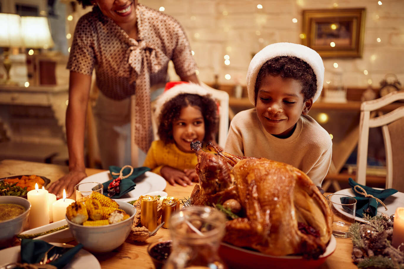 Mesa com ceia de natal, destacando o peru ao fundo a mãe e dois irmão se aproximam da comida