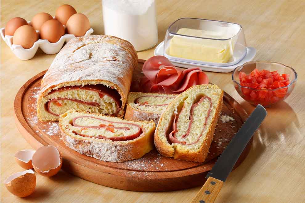 pão caseiro de mortadela em cima de uma tábua de madeira redonda com uma faca ao lado e em cima de uma mesa de madeira
