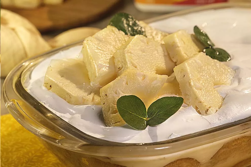Pavê de abacaxi em uma travessa retangular, sob uma mesa de madeira.