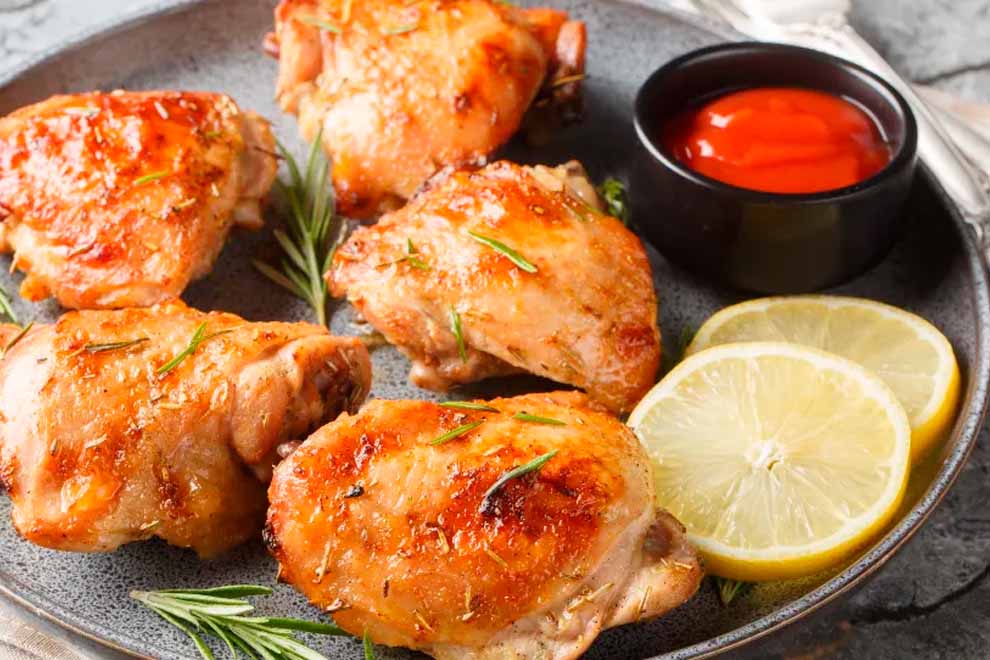 sobrecoxa temperado com batatas e cabeça de alho dentro de um prato preto de porcelana e em cima da mesa