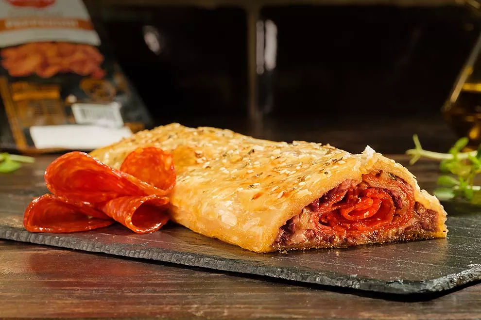 Rocambole de pepperoni em cima de uma tábua de cerâmica,  sob uma mesa de madeira.