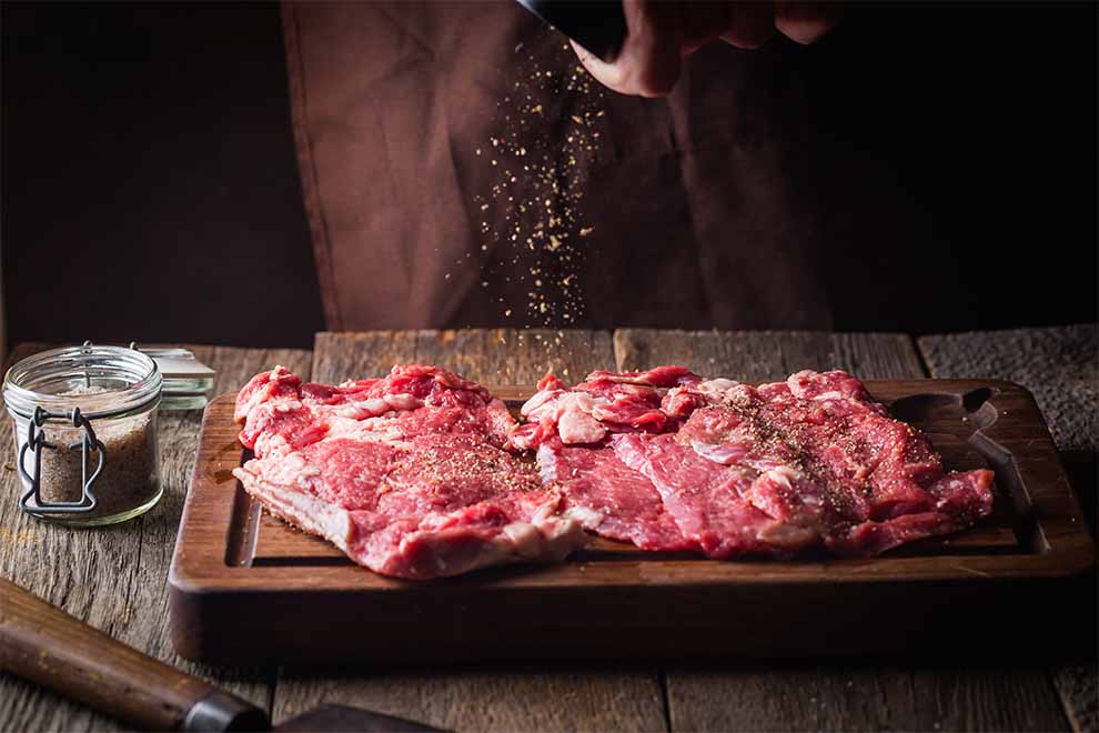 Carne sendo temperada em tábua de madeira