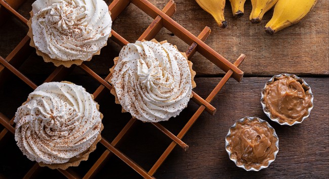 A foto mostra uma torta banoffe de banana com doce de leite servida no pote para presentear.