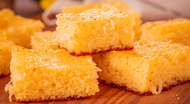 Fatias de bolo de fubá cremoso dispostos empilhados em uma tábua de madeira.