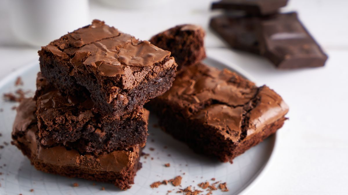 A imagem destaca 3 fatias de brownie com casquinha, servido em um prato redondo raso comum.
