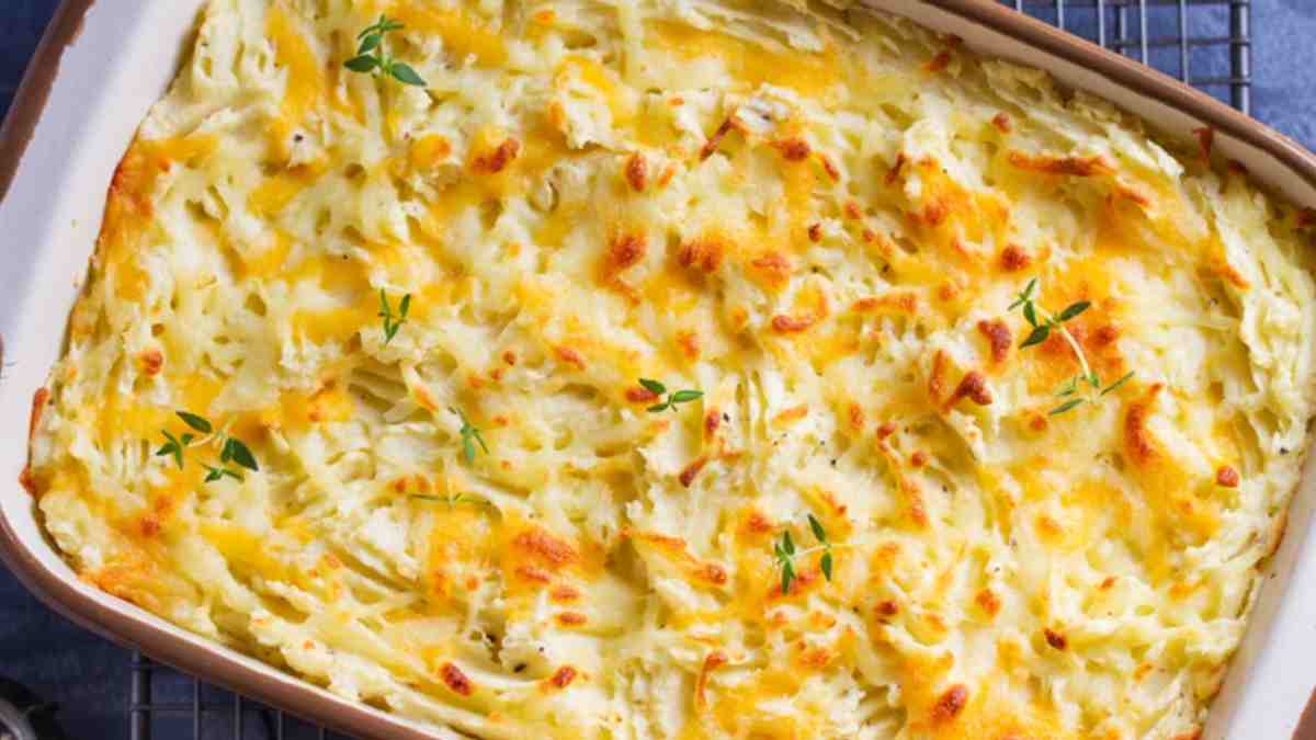 Cachorro quente de forno gratinado com queijo muçarela por cima servido em uma travessa branca.