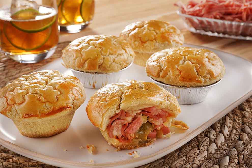 empadinha de mortadela em cima de um pequeno prato de porcelana retangular e em cima de um jogo americano redondo em palha