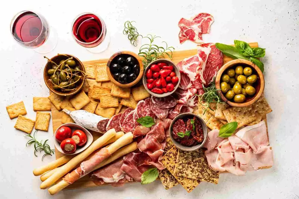 tábua de charcutaria em uma mesa branca com azeitona com vinho