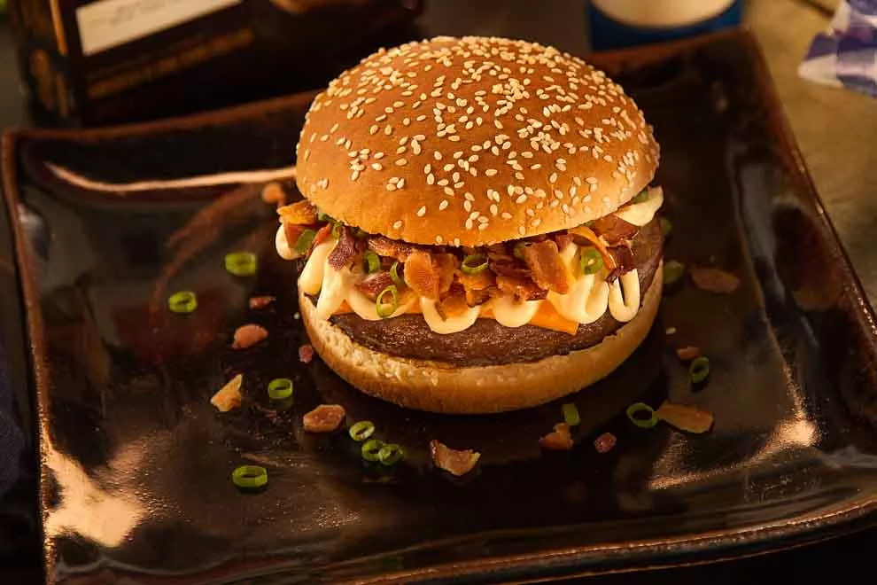 hamburguer com farofa de bacon e cebolinha dentro de um prato quadrado preto de porcelana em cima de uma mesa
