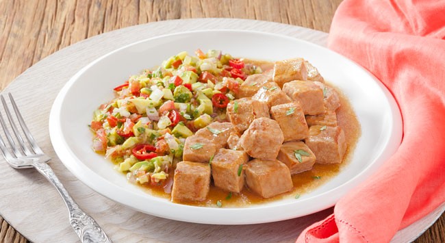 Lombo suíno em cubos servido com vinagrete de guacamole me um prato branco raso.