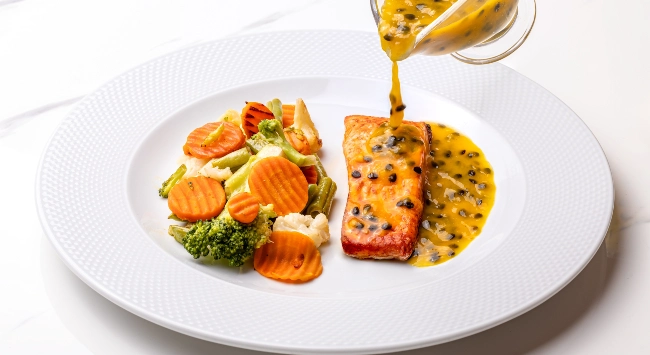 Prato branco com porção de salada e um pedaço de salmão com molho de maracujá. 