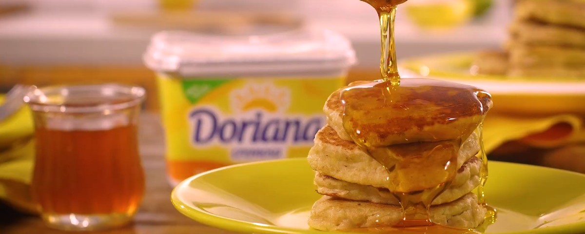 panqueca de banana com aveia servida em um prato amarelo redondo, com mel e manteiga