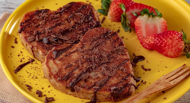 Panqueca de banana em formato de coração servida com calda de chocolate em um prato amarelo.