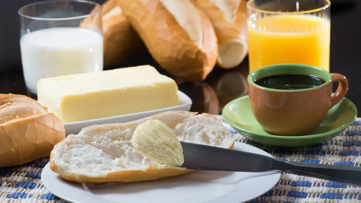 Pão francês na mesa com itens de café da manhã.