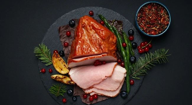 Pernil suíno assado com batatas disposto em uma tábua de madeira preta.