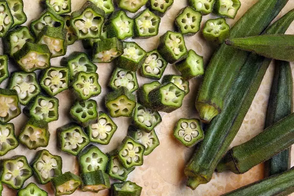 Imagem de diversos Quiabos sob uma mesa laranja, com alguns deles cortados em pedaços.