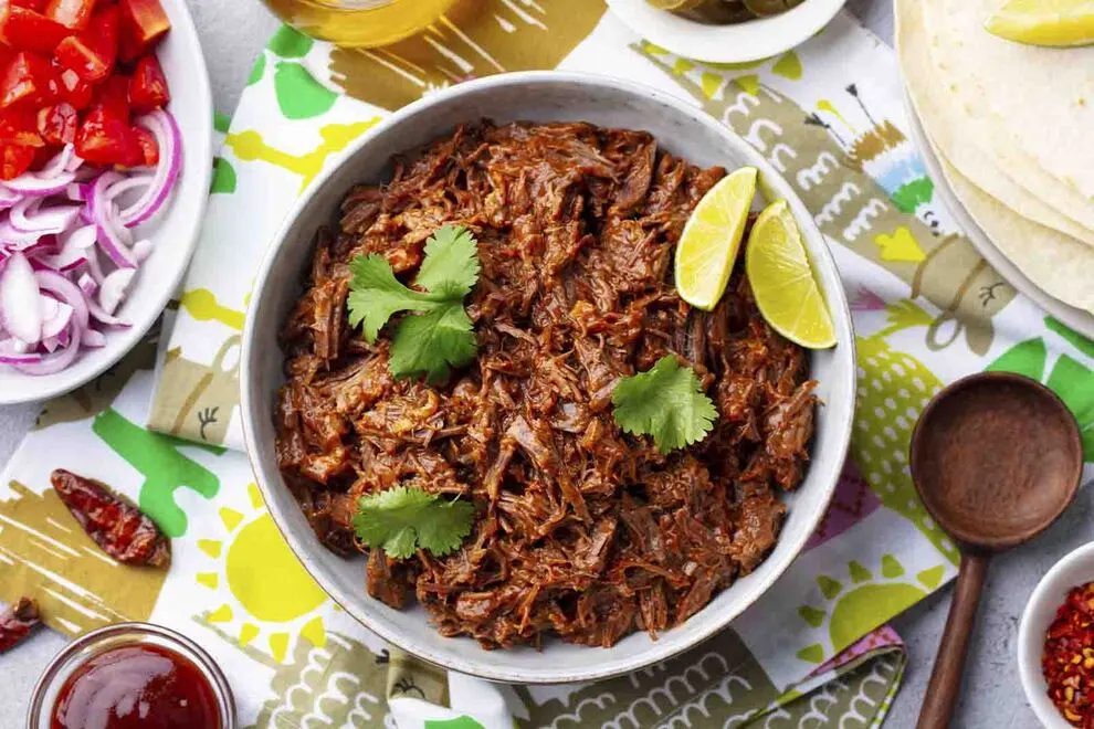 Imagem de um Ragu, com duas fatias de limão e três ramos de salsinha, em cima de uma tigela branca funda, com diversos ingrediente ao redor, sob uma mesa com diversos panos dobrados por cima, com uma vista de cima