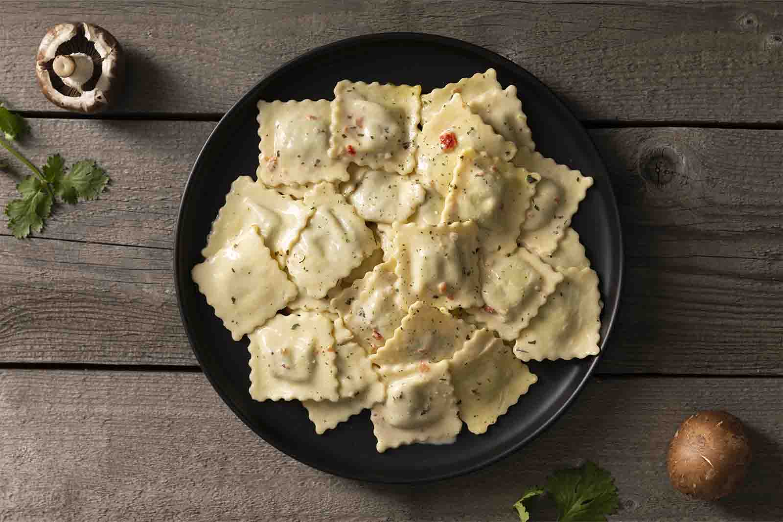 Imagem de um prato de ravioli ao molho branco visto de cima sob a mesa